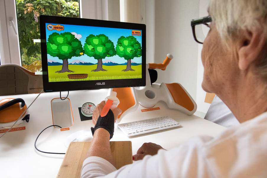 Eine ältere Frau bedient mit ihrer Hand an einem Computer einen Bildschirm
