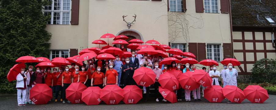 Mitarbeiter der GLG Fachklinik Wolletzsee vor dem ehemaligen Jagdschloss mit roten Schirmen.