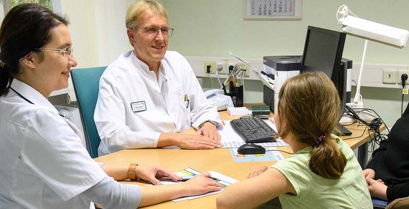 Foto: Zwei Mediziner am Tisch mit einem Kind