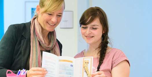 Foto: Eine Therapeutin und ein Mädchen schauen gemeinsam auf ein Faltblatt